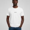 Male model wearing a white FLIPN t-shirt with minimalist logo text, paired with blue jeans.